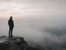 Homem observando horizonte encoberto por neblina enquanto apenas parte da paisagem está visível.