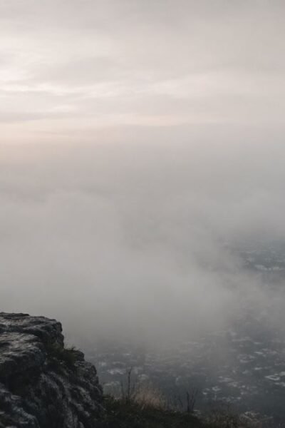 Homem observando horizonte encoberto por neblina enquanto apenas parte da paisagem está visível.